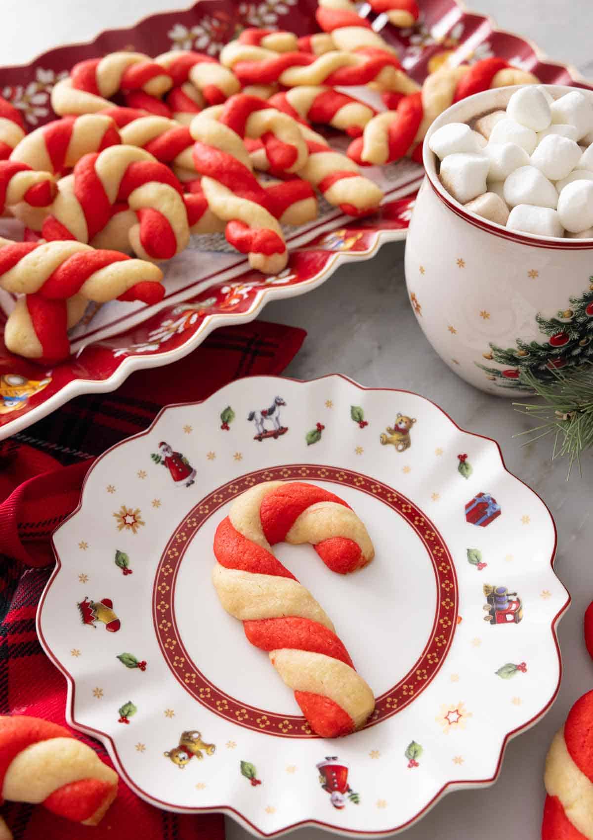 A plate with a candy cane cookie in front of a platter of them.
