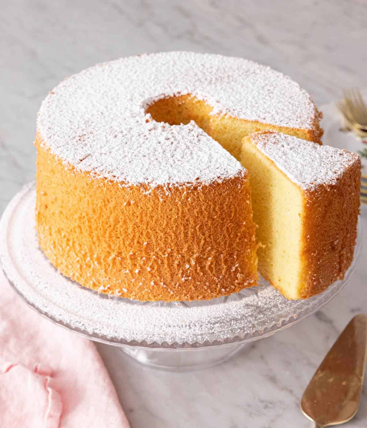 A chiffon cake dusted with powdered sugar with a slice cut and pulled forward.