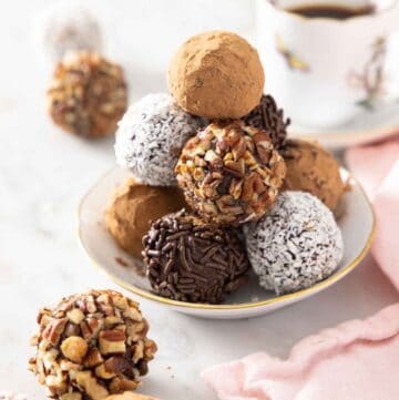 A plate with a pile of chocolate truffles with different coatings. A few in front.