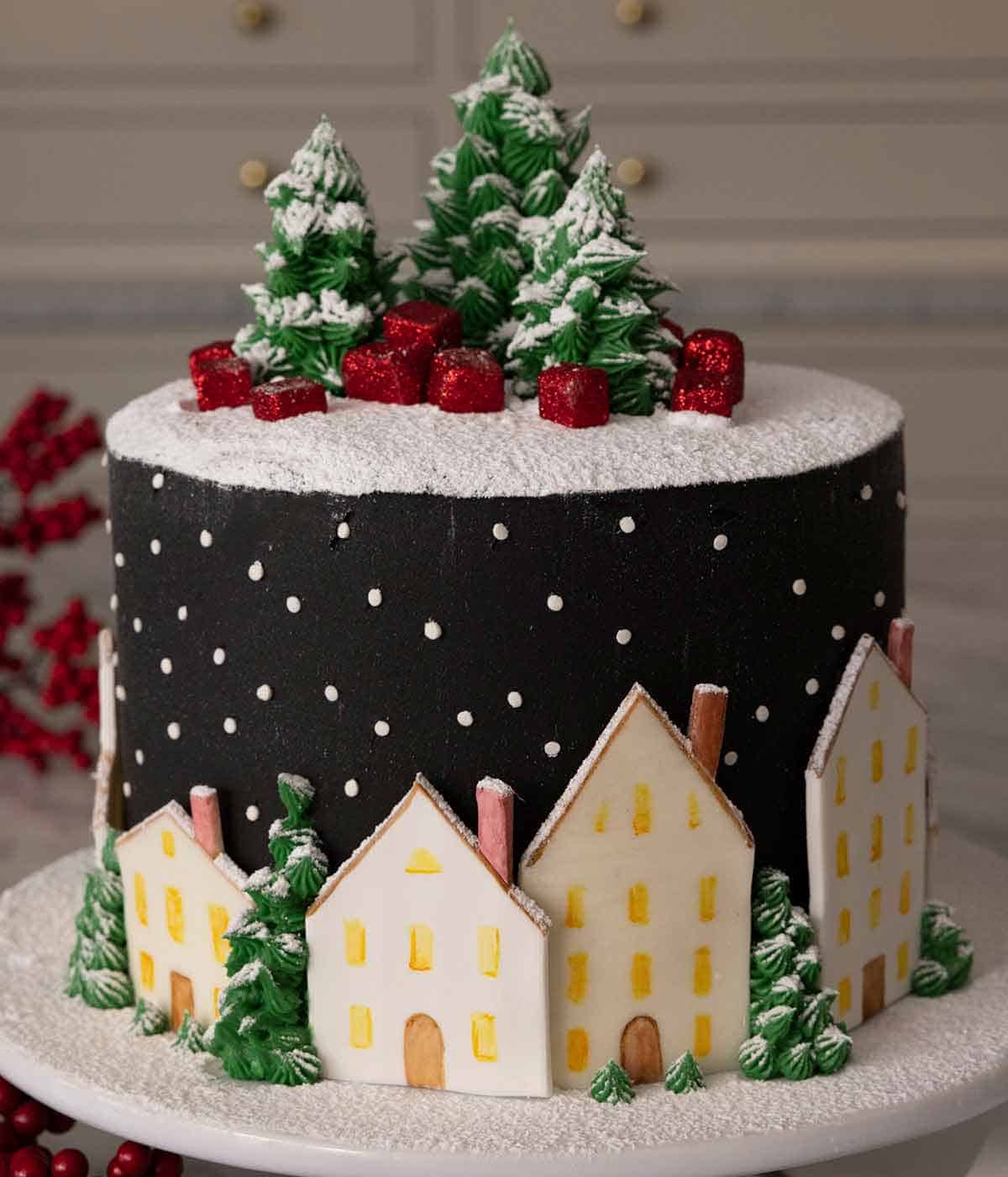 A cake decorated with a starry sky frosting with decorative houses, trees, and gifts.