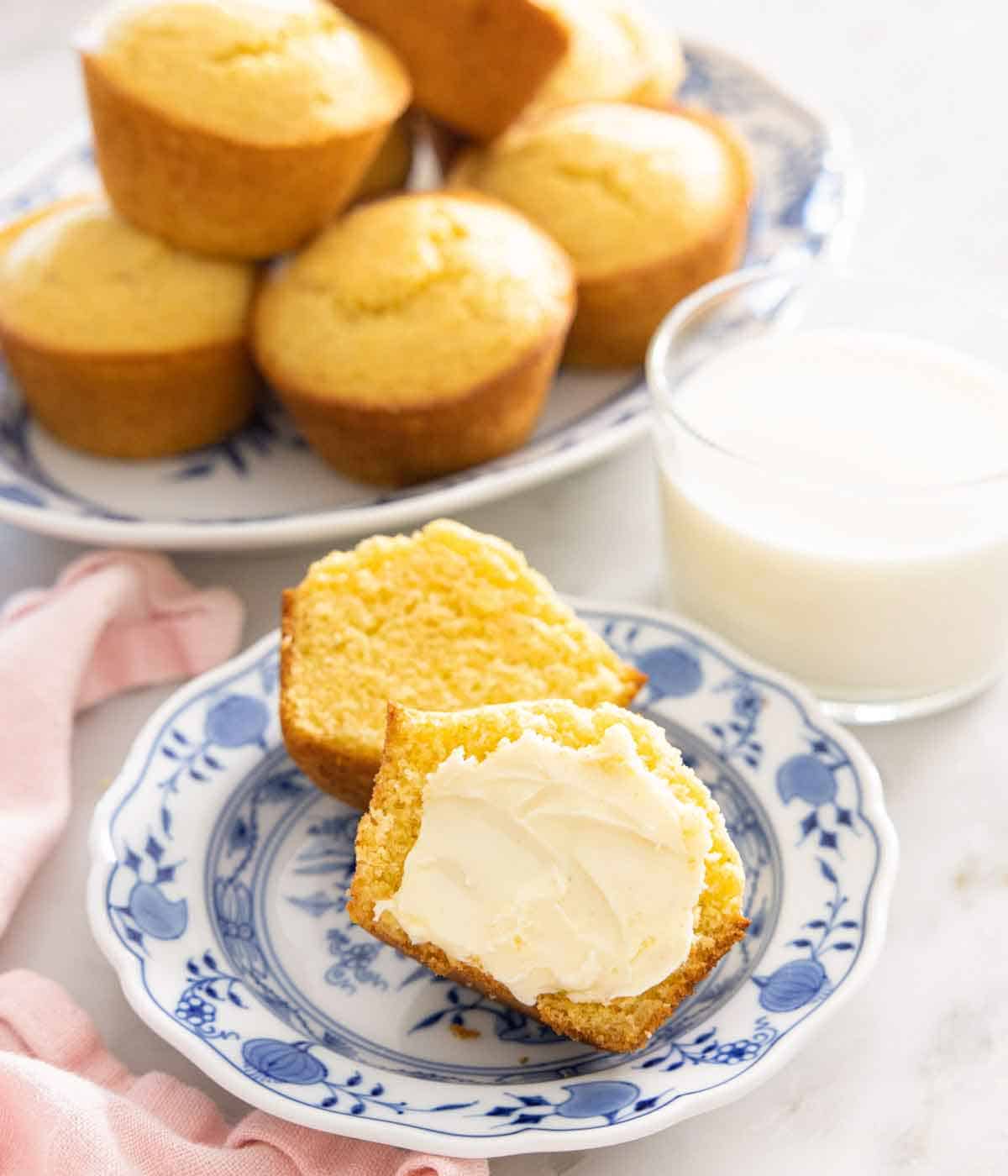 A plate with a cornbread muffin cut in half with butter spread on it.