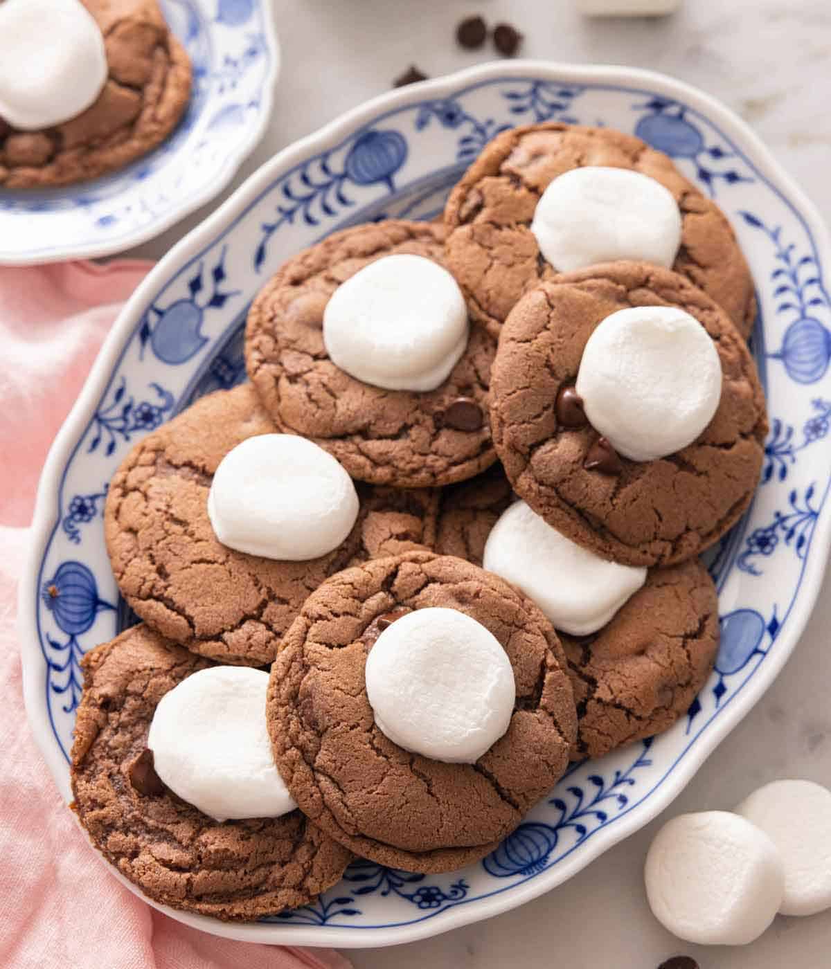 A platter with multiple hot chocolate cookies with marshmallows and chocolate chips scattered around.