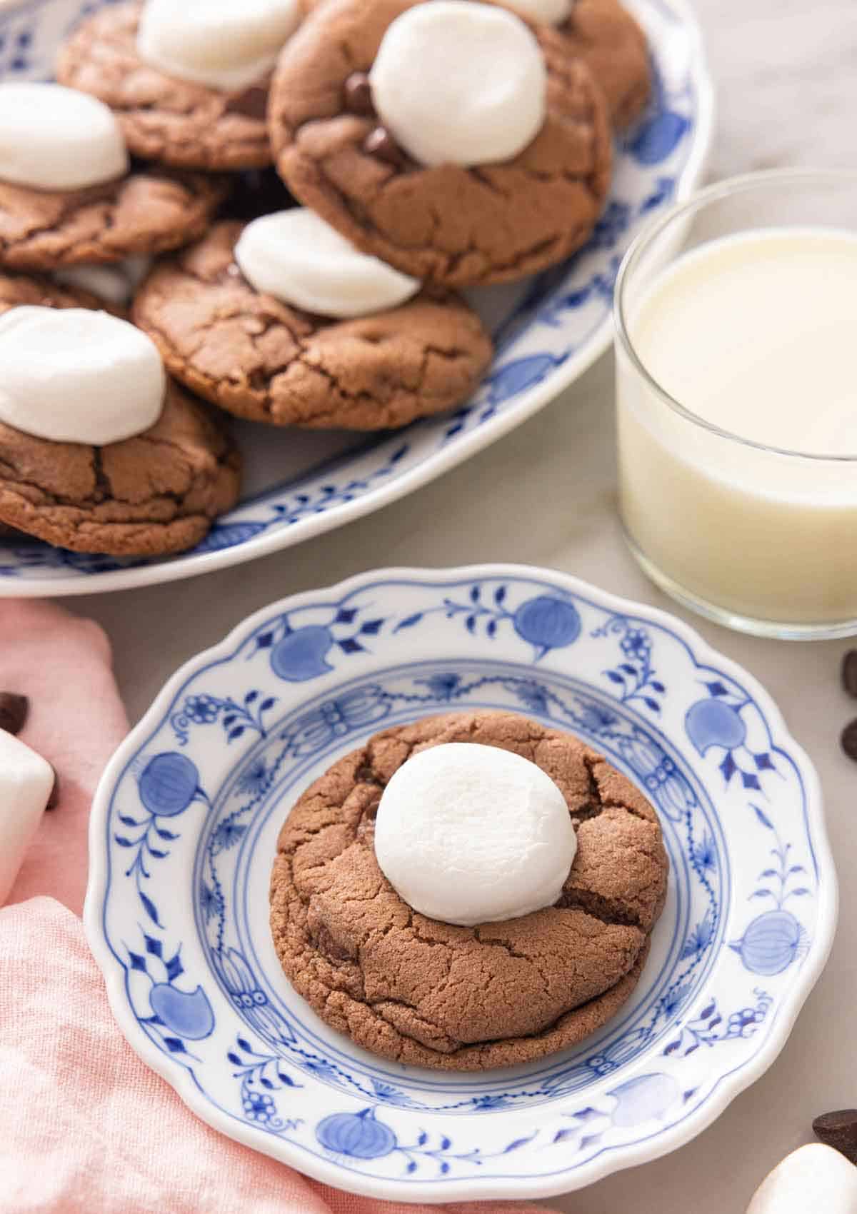 A plate with a hot chocolate cookies in front of a glass of milk.
