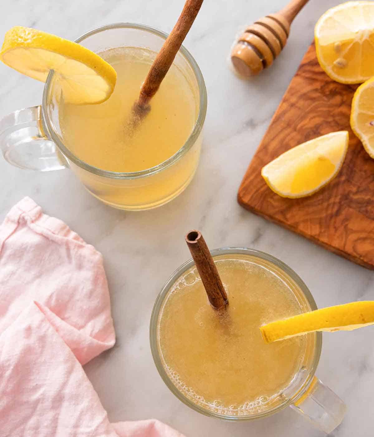 Overhead view of two glasses of hot toddies with cut lemon and honey on the side.