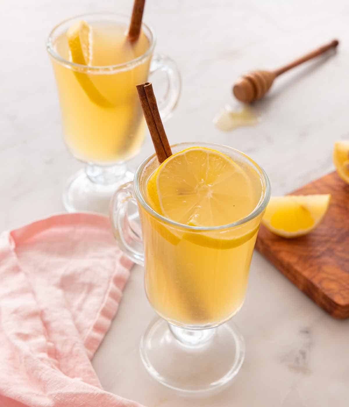 Two cups of hot toddies with lemon and cinnamon stick in the cups.