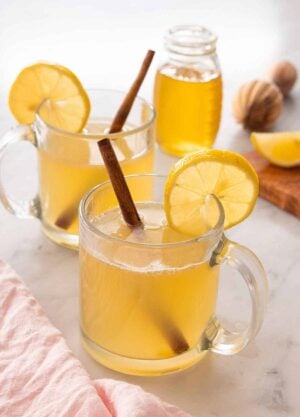A glass of hot toddy in front of a second on and a jar of honey.