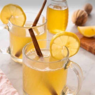 Pinterest graphic of two glasses of hot toddies with lemon slices and cinnamon sticks.