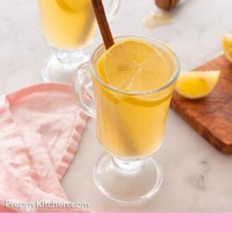 Pinterest graphic of two glasses of hot toddies with lemon slices and cinnamon sticks inside.
