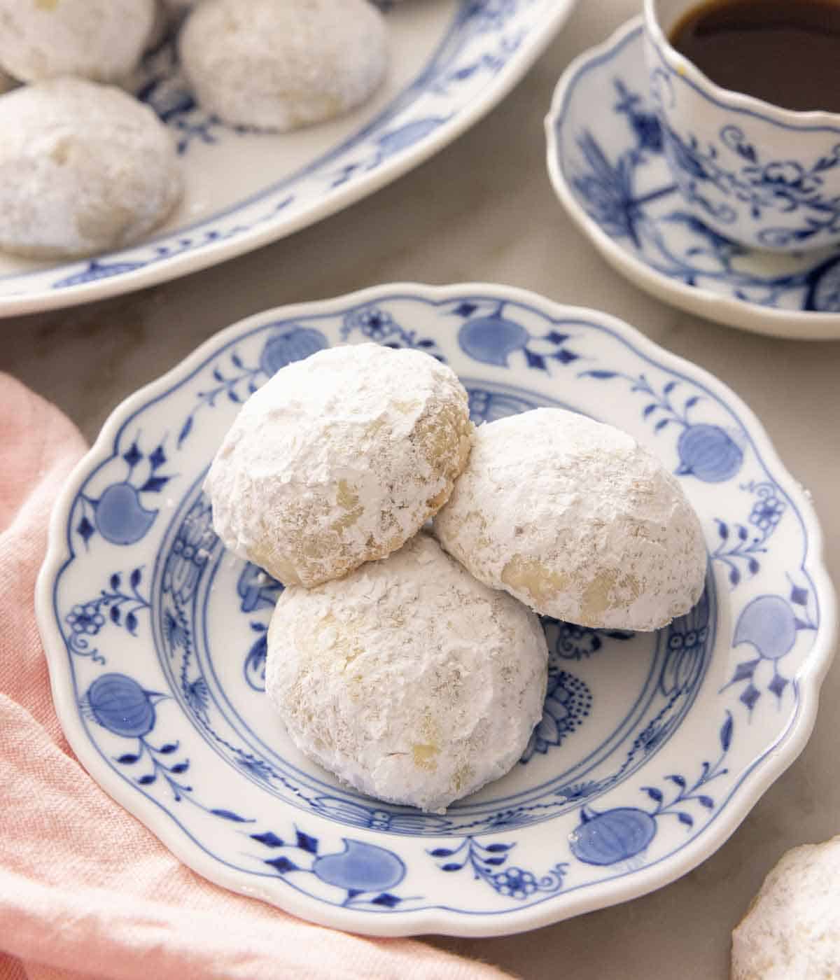 A plate with three Mexican wedding cookies by a cup of coffee.