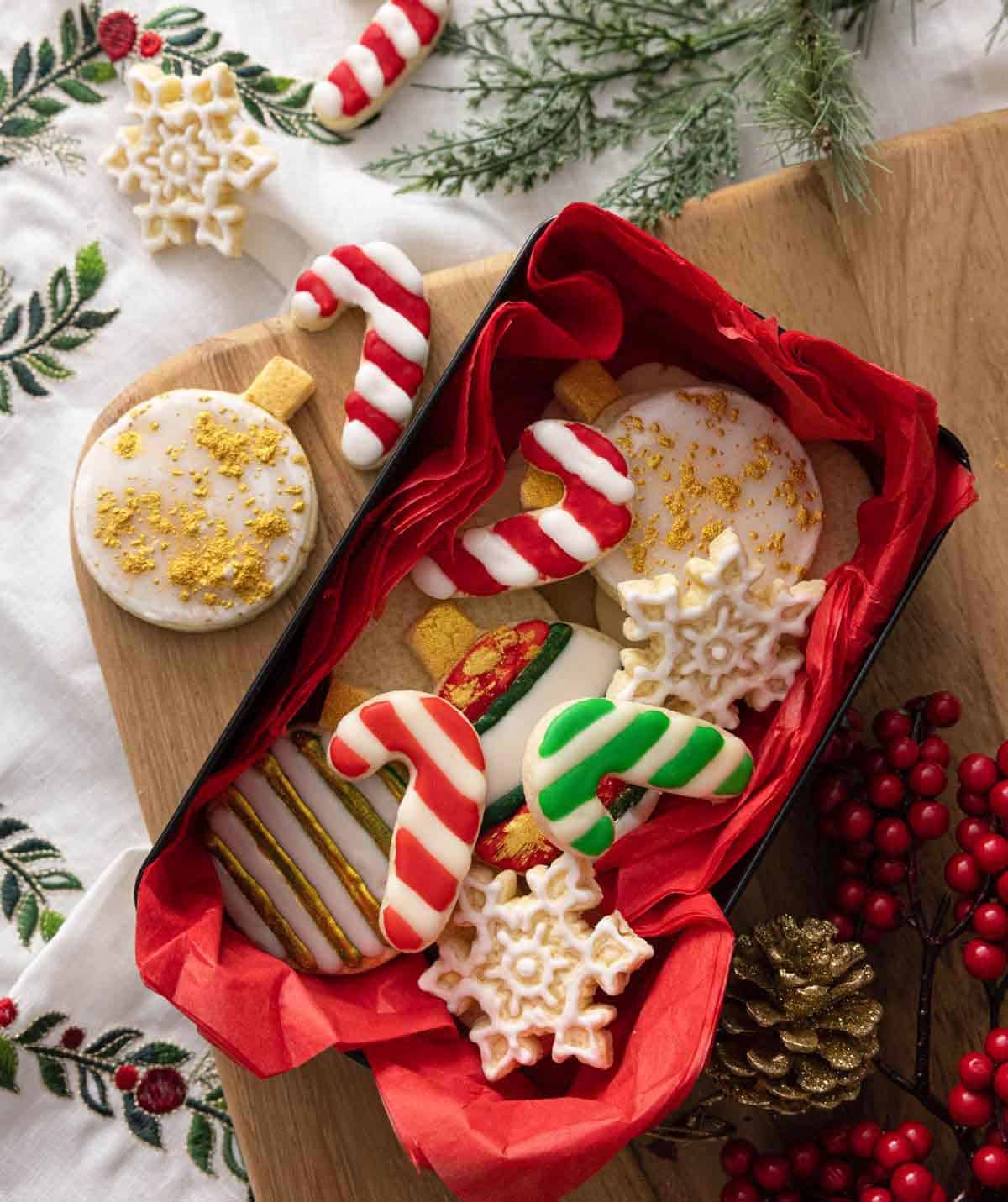 A lined box with multiple cookies shaped as ornaments, candy cane, and snowflakes.