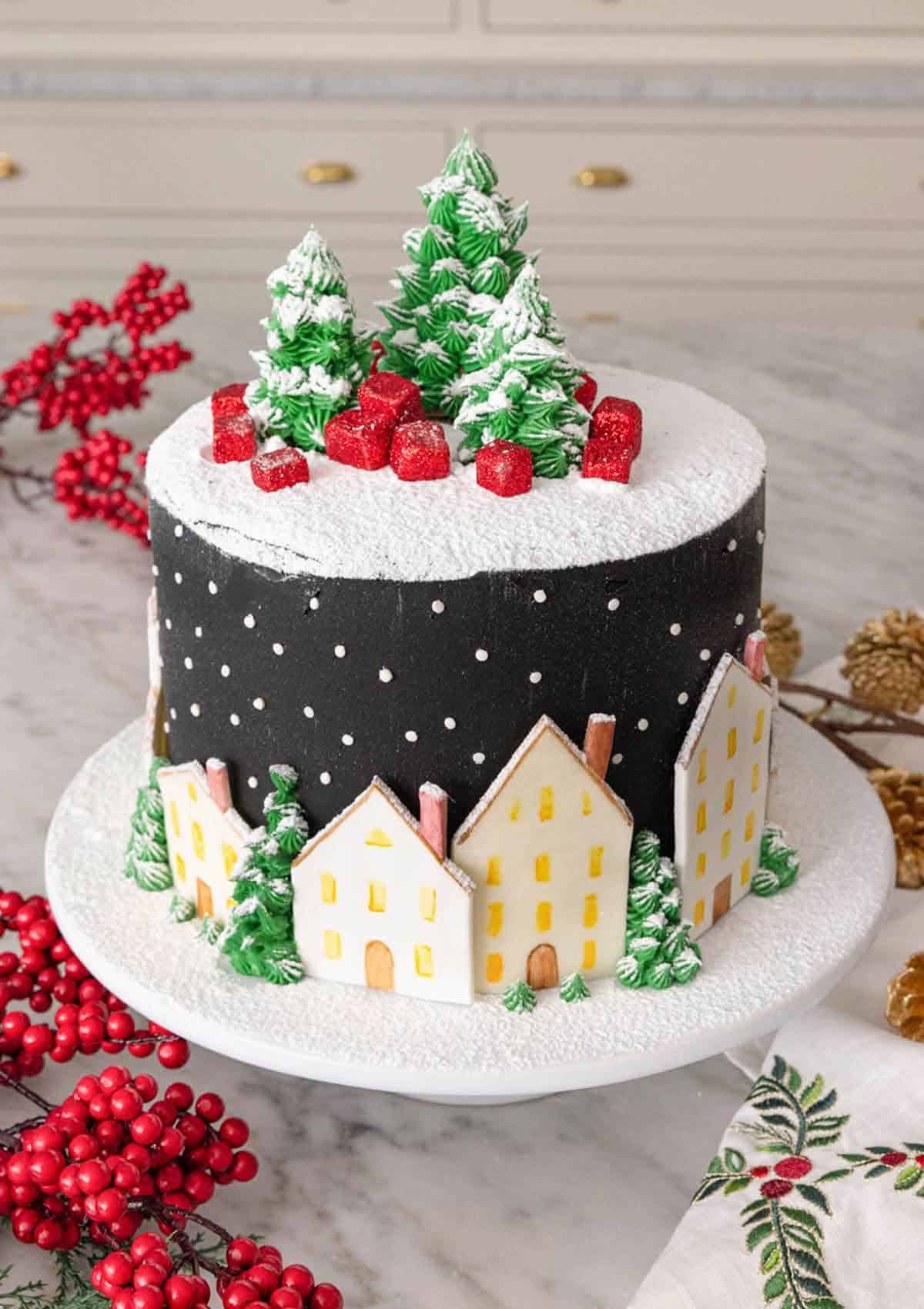 A cake decorated with houses, trees, and presents with a starry night frosting.