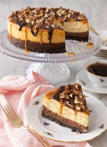 A turtle cheesecake on a cake stand with a slice in front.