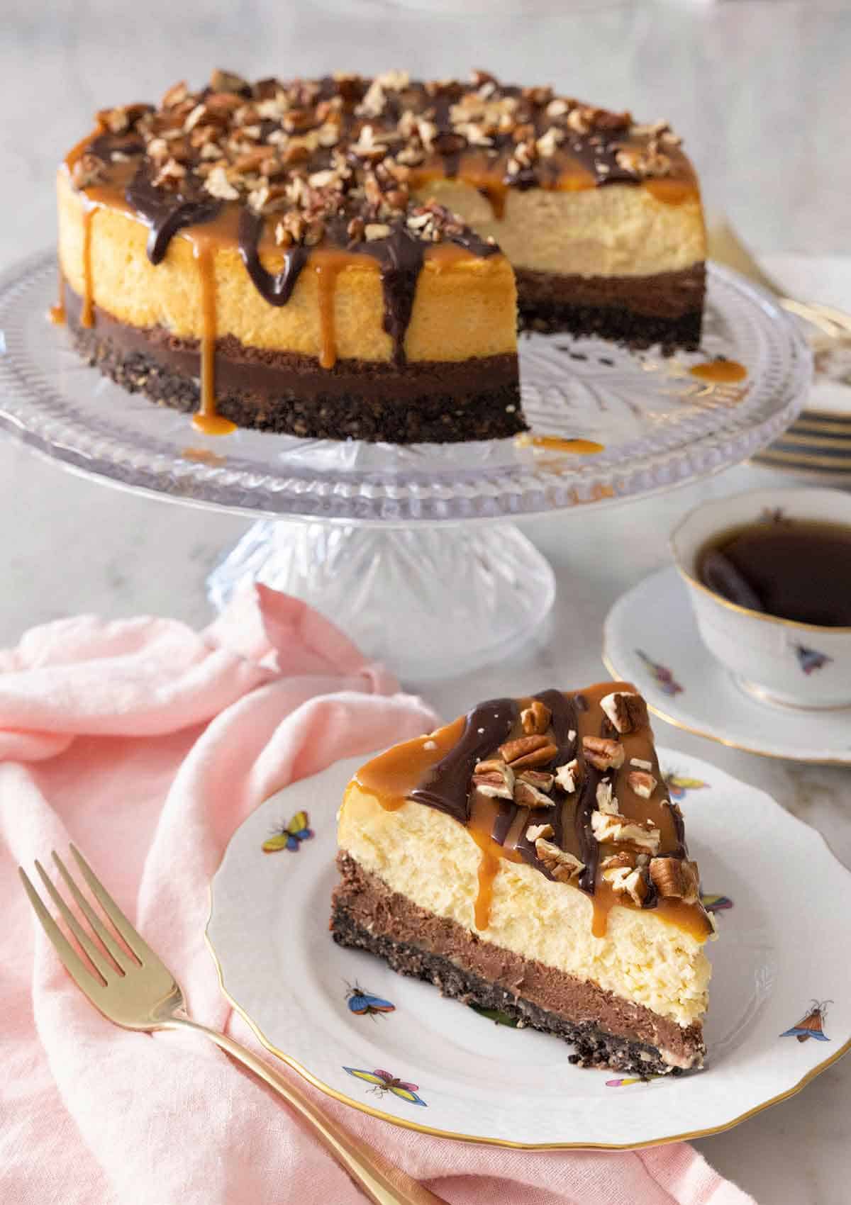 A turtle cheesecake on a cake stand with a slice in front.