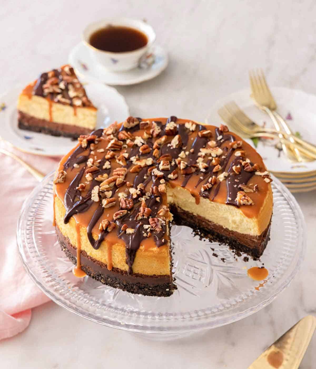 A turtle cheesecake with a slice cut and plated in the back.