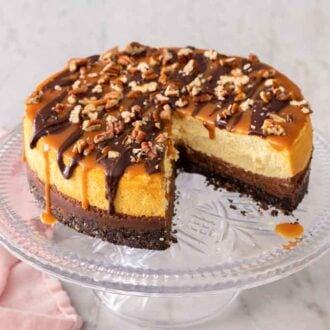 A turtle cheesecake with a slice cut out, on a cake stand.