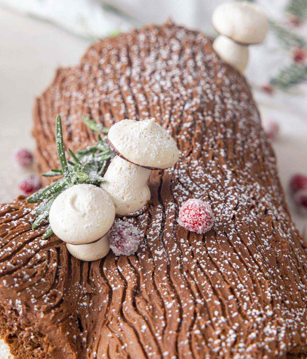 Close up of decorative mushrooms, sugared cranberries, and rosemary on a Buche de Noel.