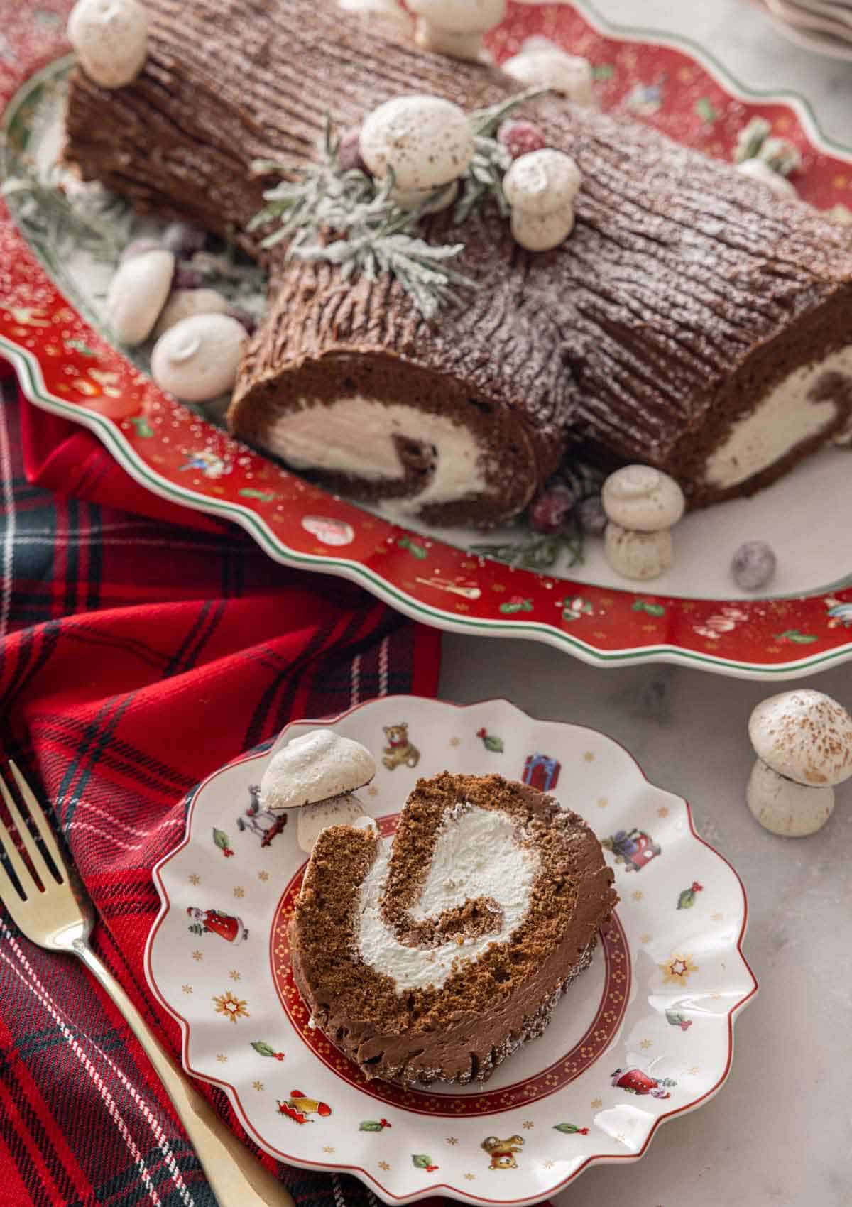 A Yule log on a platter with a slice of the cake on a plate in front of it.