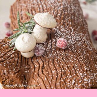 Pinterest graphic of the close up of a Yule log with meringue mushrooms, sugared cranberries, and rosemary on top.