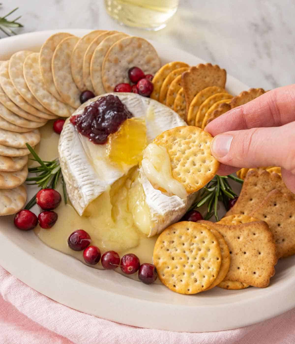 A cracker scooping out melty baked brie from the platter.