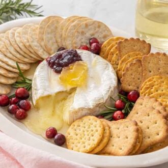 A platter with crackers, baked brie, honey, and jam.