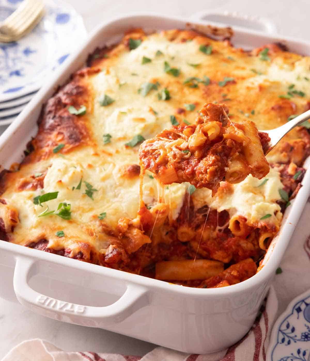 A white baking dish with baked ziti with a spoonful lifted out.