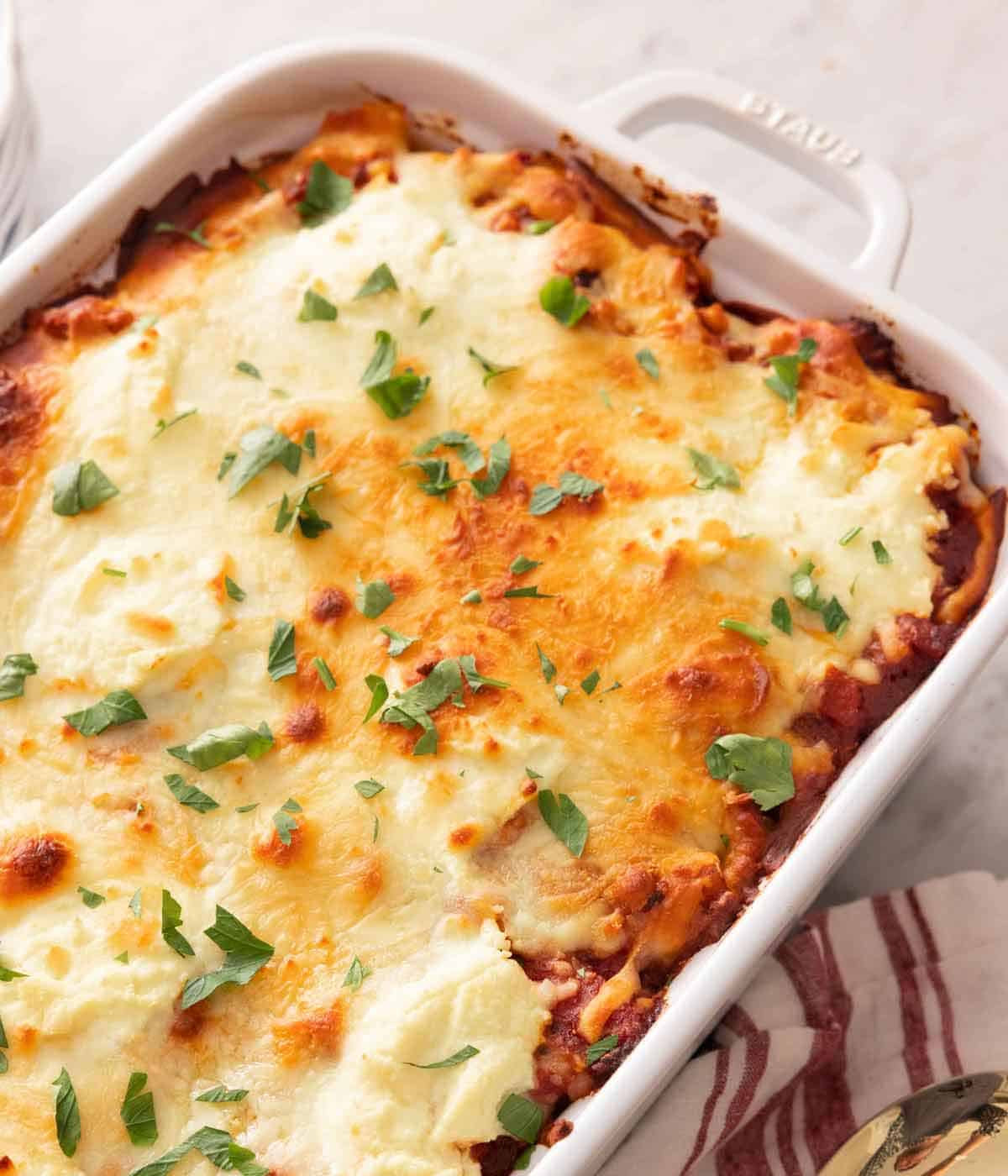 A white baking dish of baked ziti with fresh herb garnish on top.