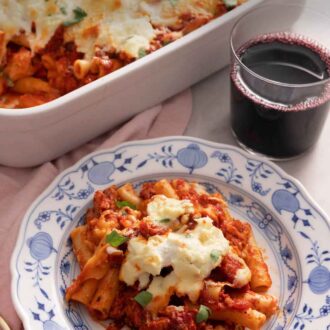 Pinterest graphic of a plate with a serving of baked ziti by a glass of wine.