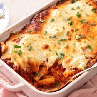 A baking dish with baked ziti with a spoon tucked into the pasta.