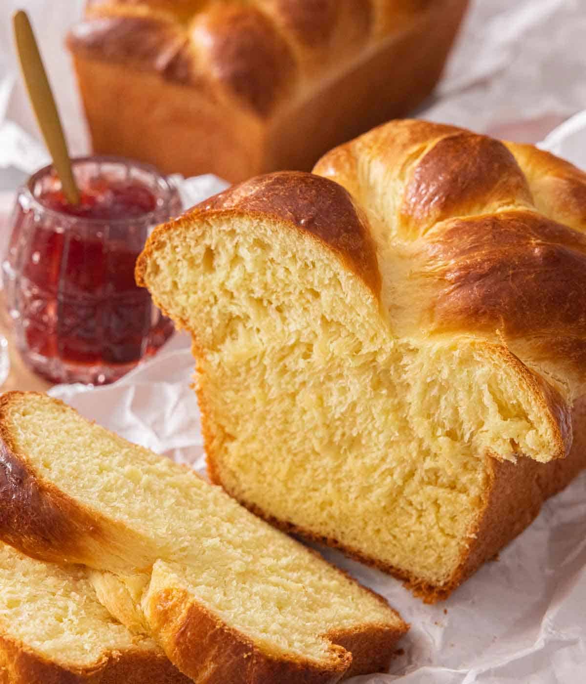 A loaf of sliced brioche bread with a jar of jam in the background.