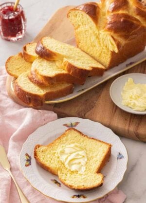 A slice of brioche bread with butter on it, in front of a sliced loaf.