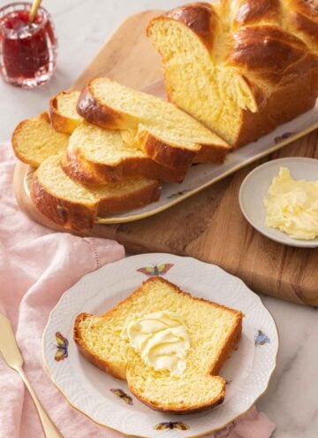 A slice of brioche bread with butter on it, in front of a sliced loaf.