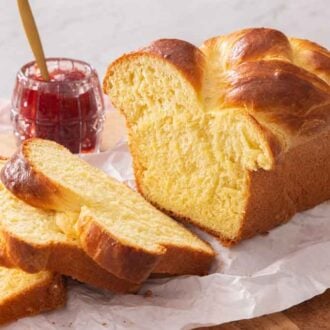 A loaf of brioche bread with three slices cut, in front, by a jam of jam.