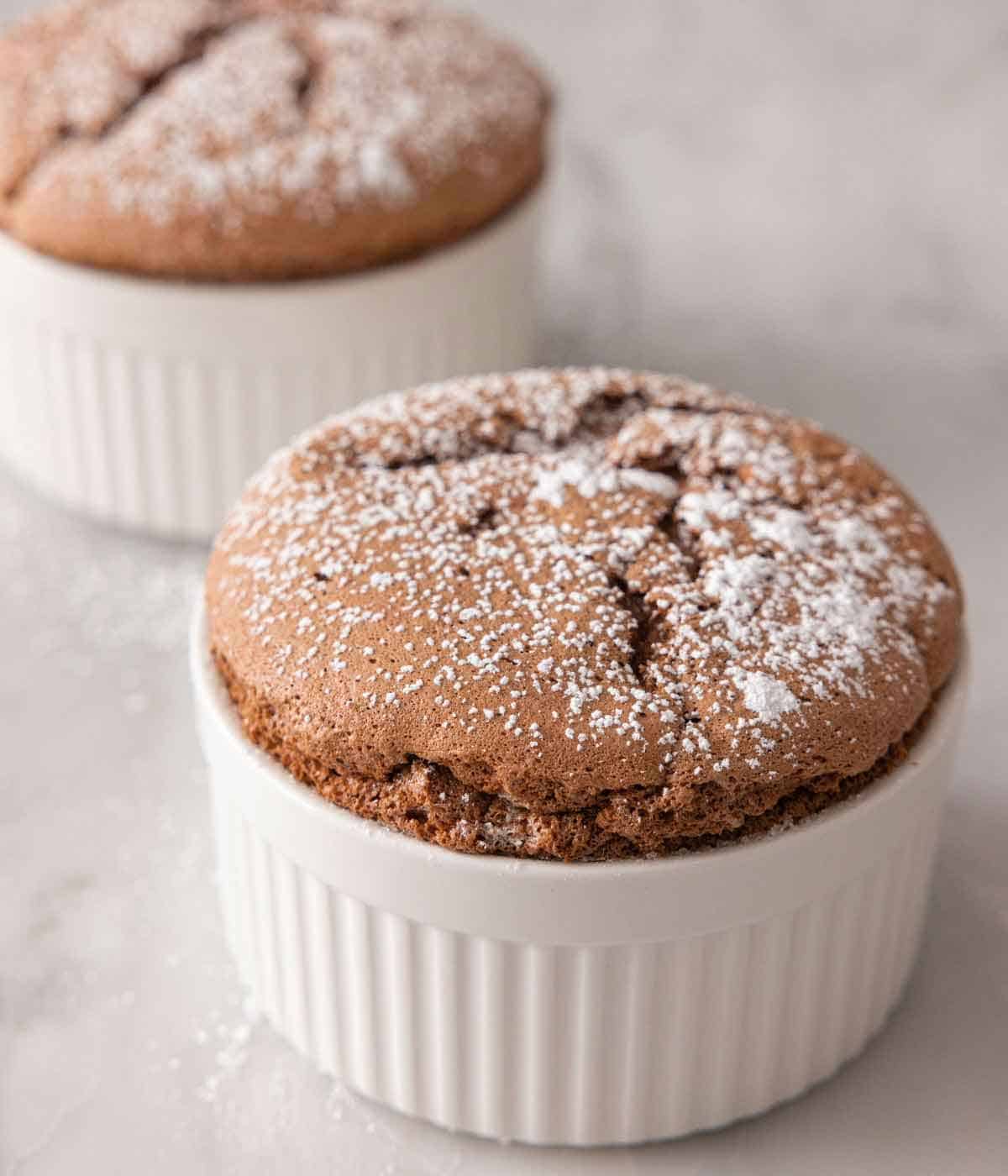 A chocolate souffle with powdered sugar in front of a second one.