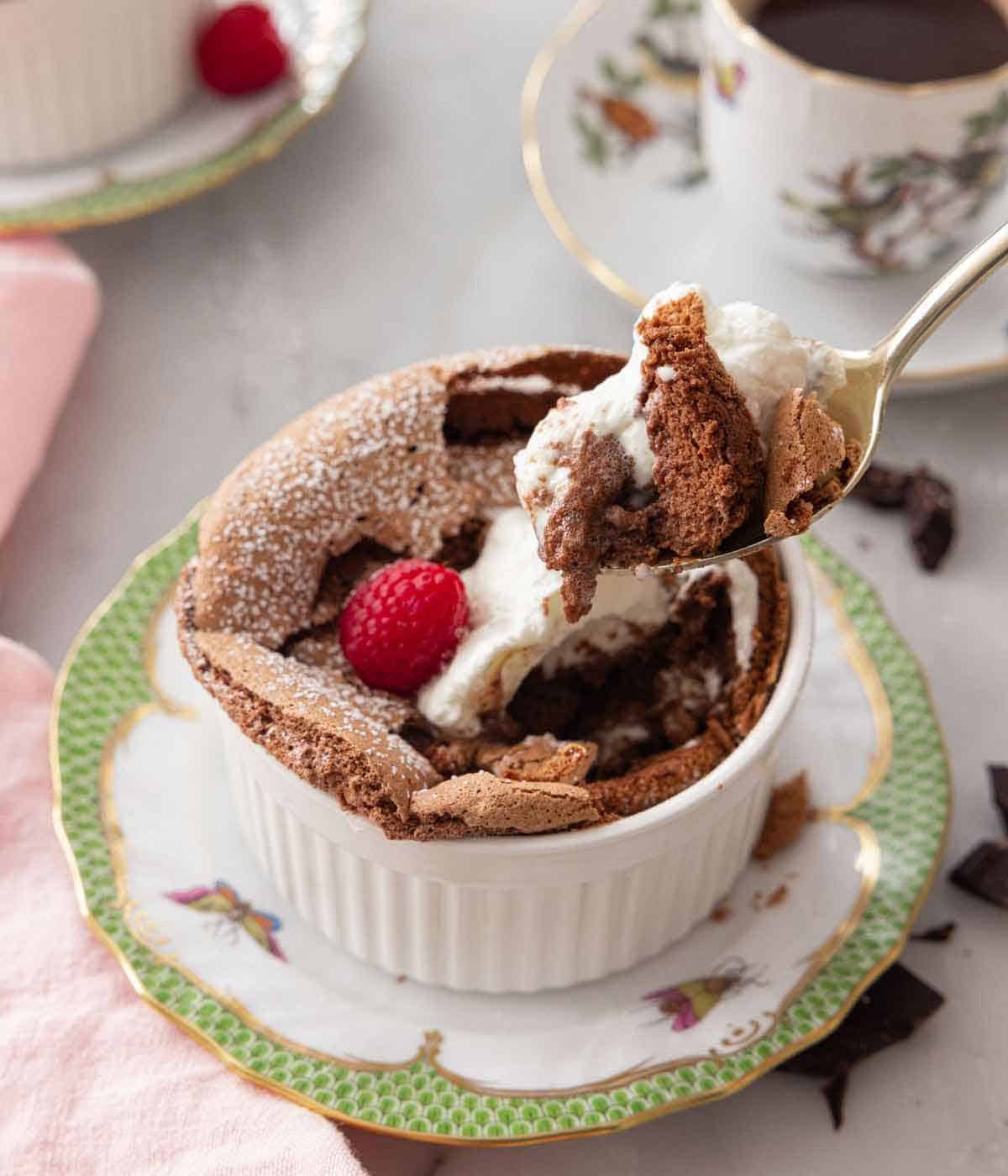 A spoonful of chocolate souffle lifted from a ramekin with a raspberry on top.