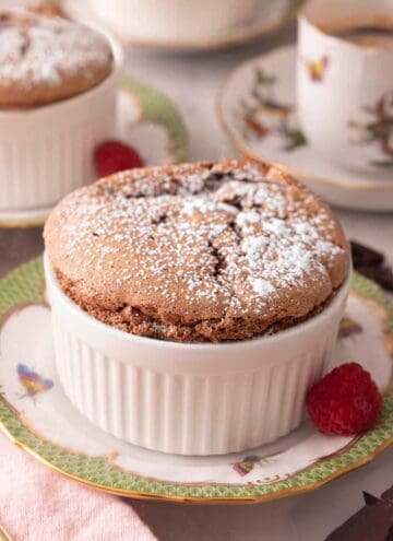 A ramekin of chocolate souffle with powdered sugar on top with a raspberry beside it.