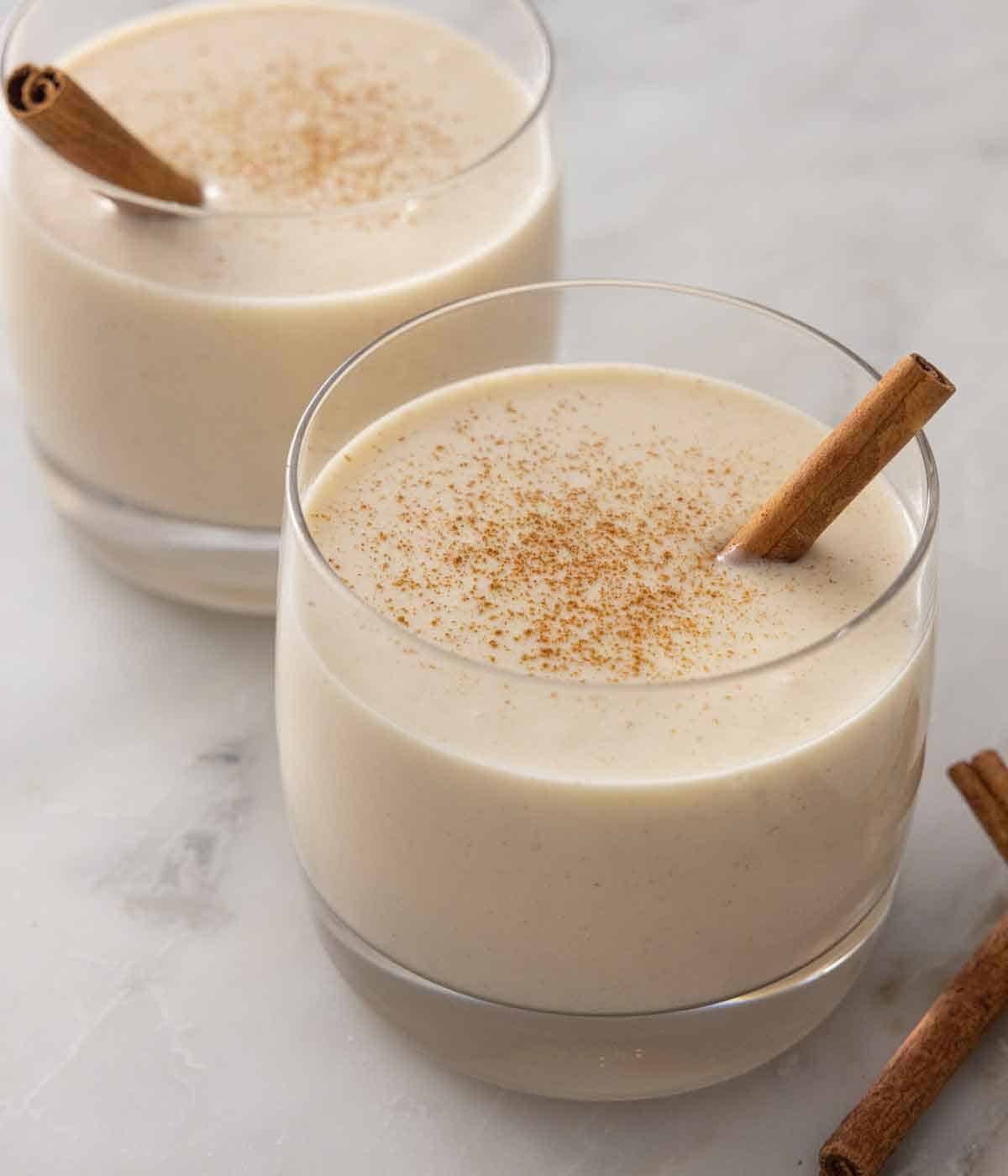 Two glasses of coquito with cinnamon sticks as garnish.