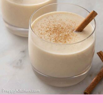 Pinterest graphic of two glasses of coquito with cinnamon dusted on top.