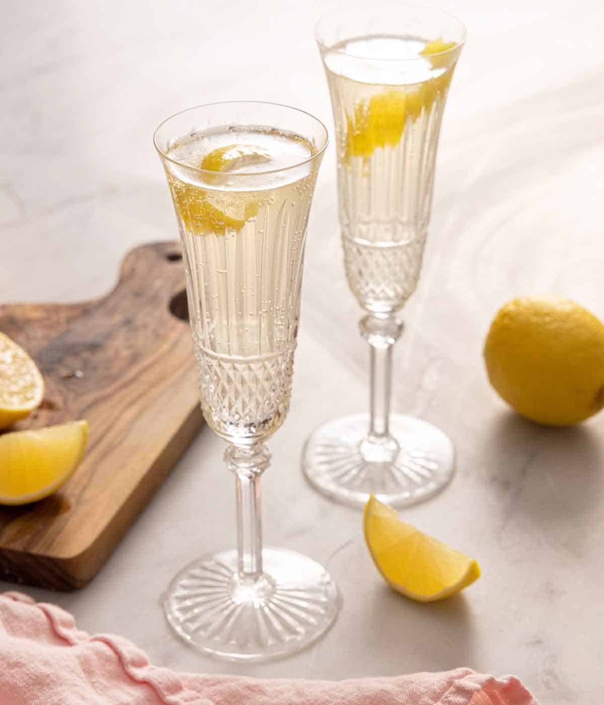 Two champagne flutes of French 75 by some freshly cut lemon wedges.