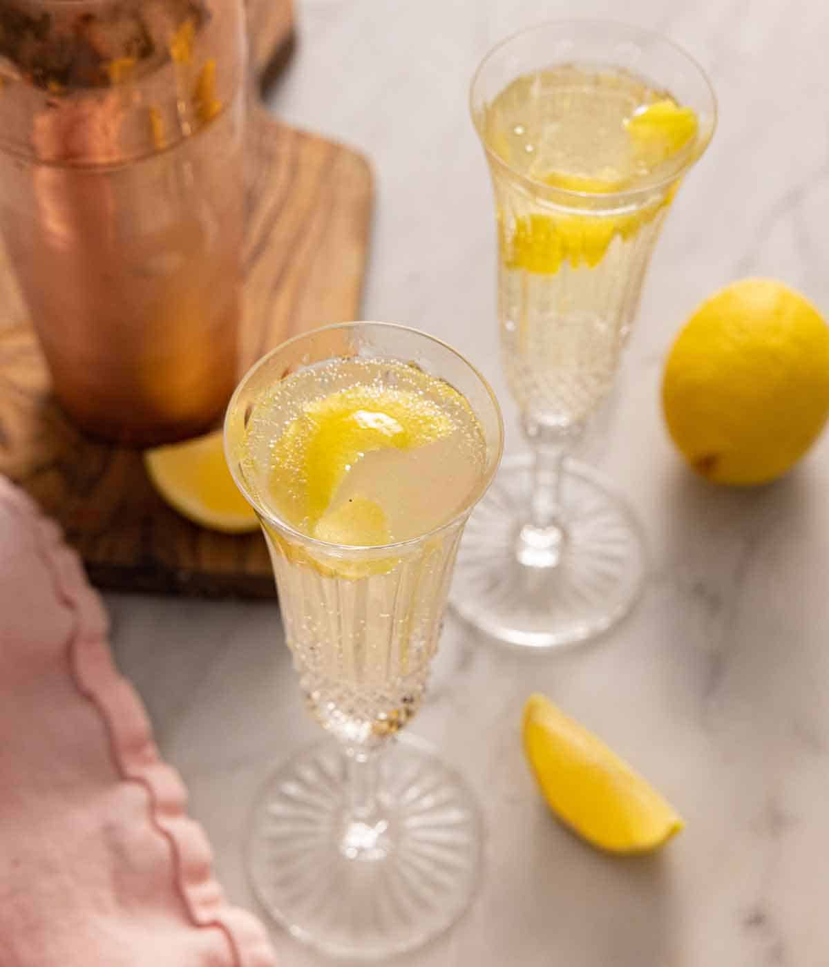 Overhead view of two glasses of French 75 with lemon peel garnishes.