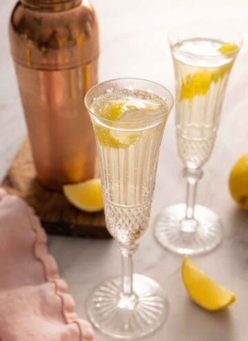 Two champagne flutes with French 75 with a lemon twist garnish.