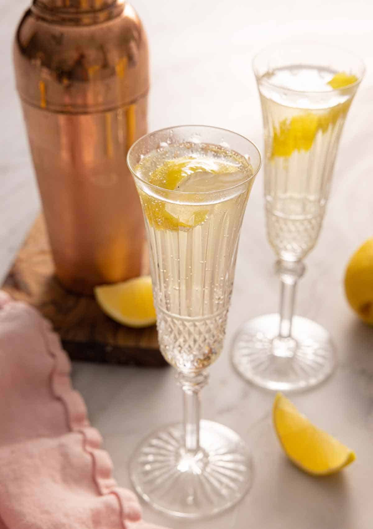 Two champagne flutes with French 75 with a lemon twist garnish.