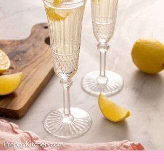 Pinterest graphic of two glasses of French 75 by some freshly cut lemons.