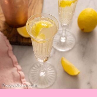 Pinterest graphic of an overhead view of two glasses of French 75 with lemon peel garnishes.
