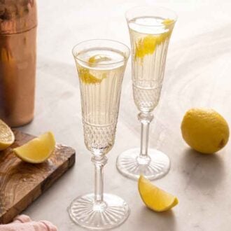 Two glasses of French 75 by a cutting board with lemons, cocktail shaker, and gin.