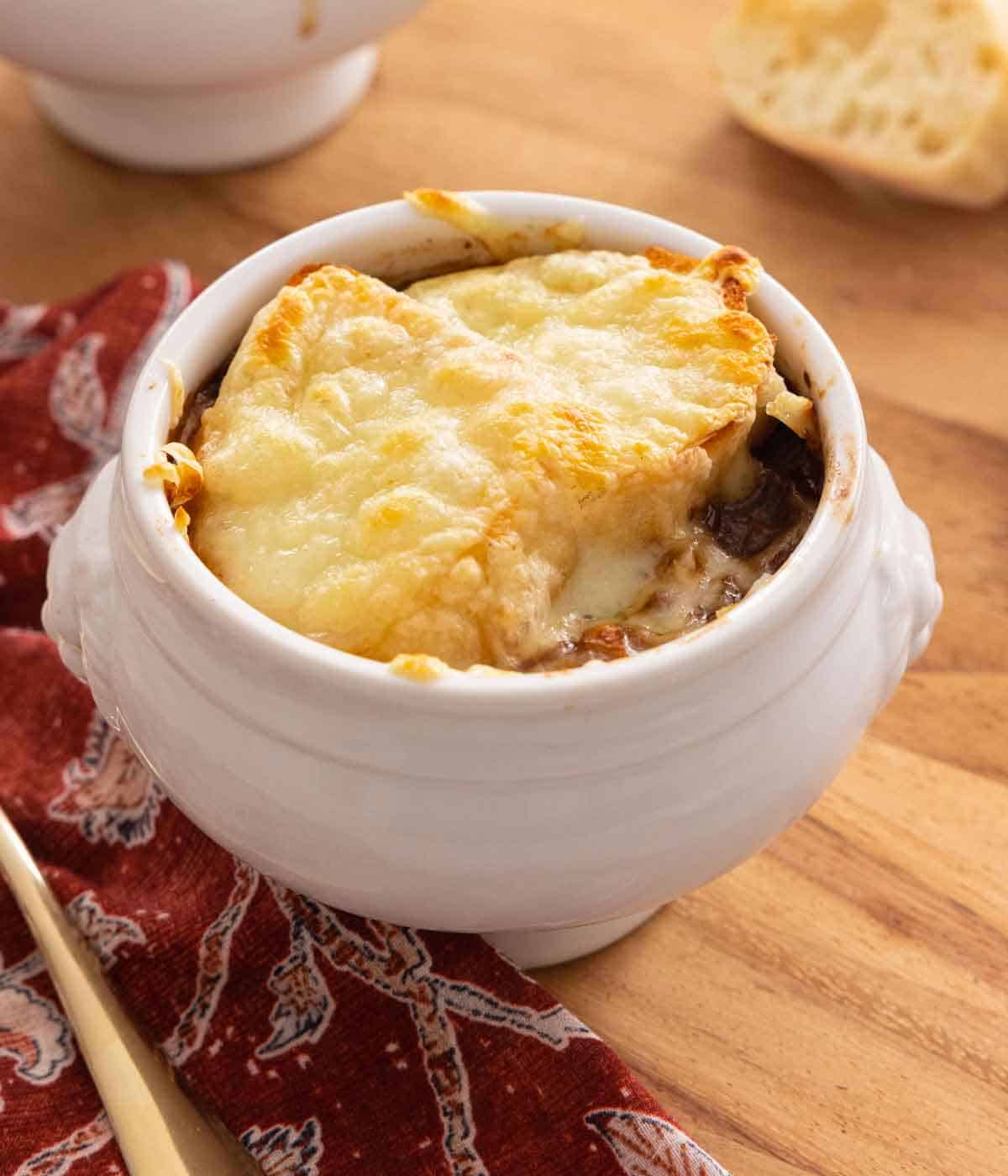 A bowl of French onion soup with a red linen beside it.
