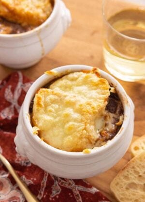 A serving of French onion soup with a glass of wine in the back.