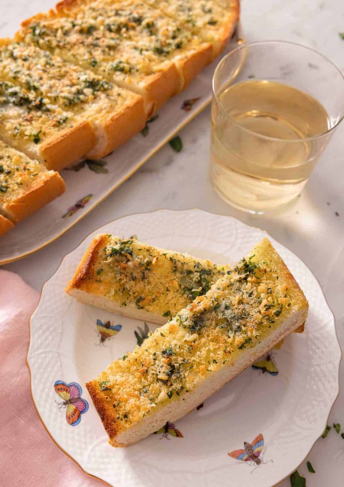 A plate with two pieces of garlic bread by a glass of wine.