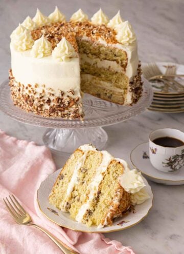 An Italian cream cake on a cake stand with a slice served in front.