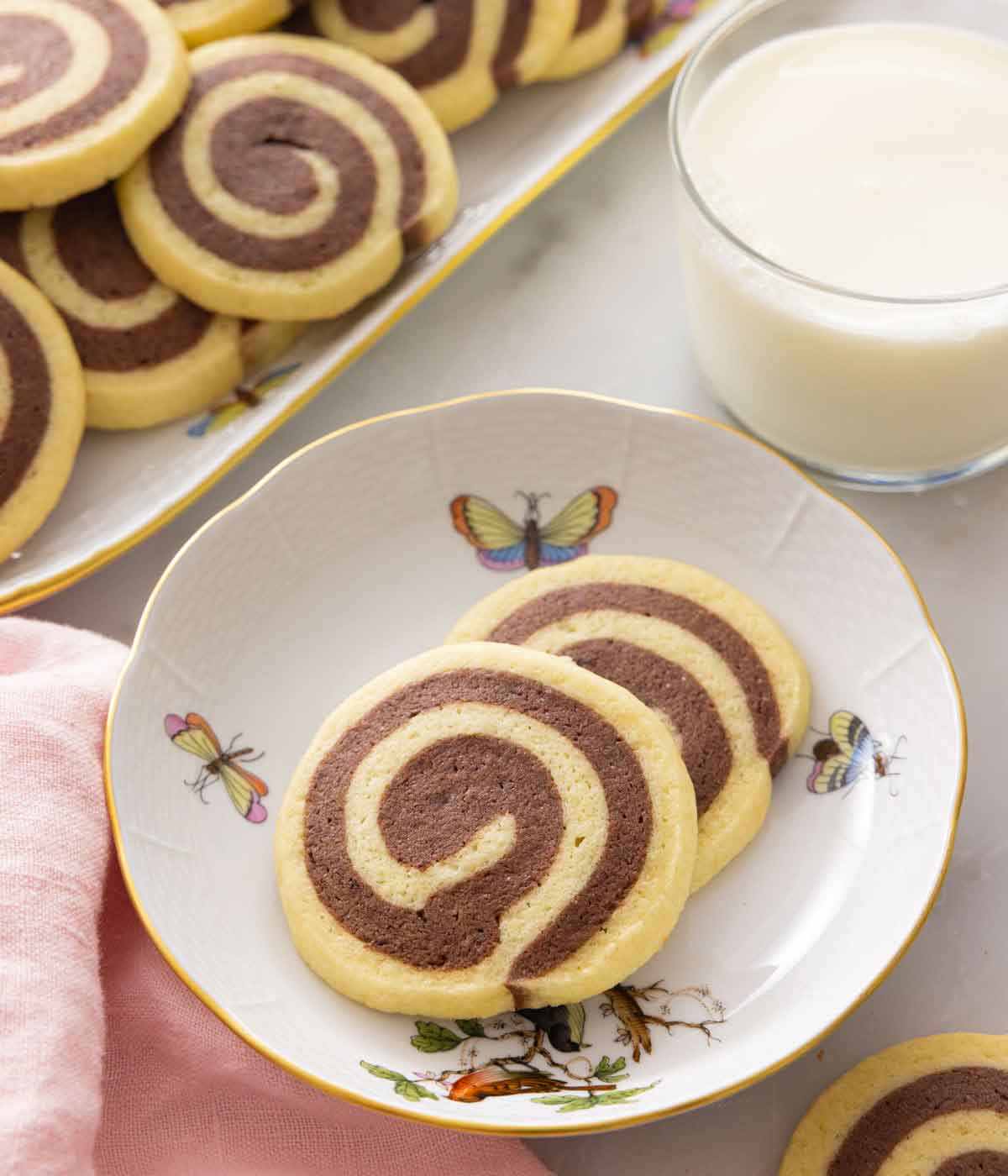 A plate with two pinwheel cookies by a glass of milk.