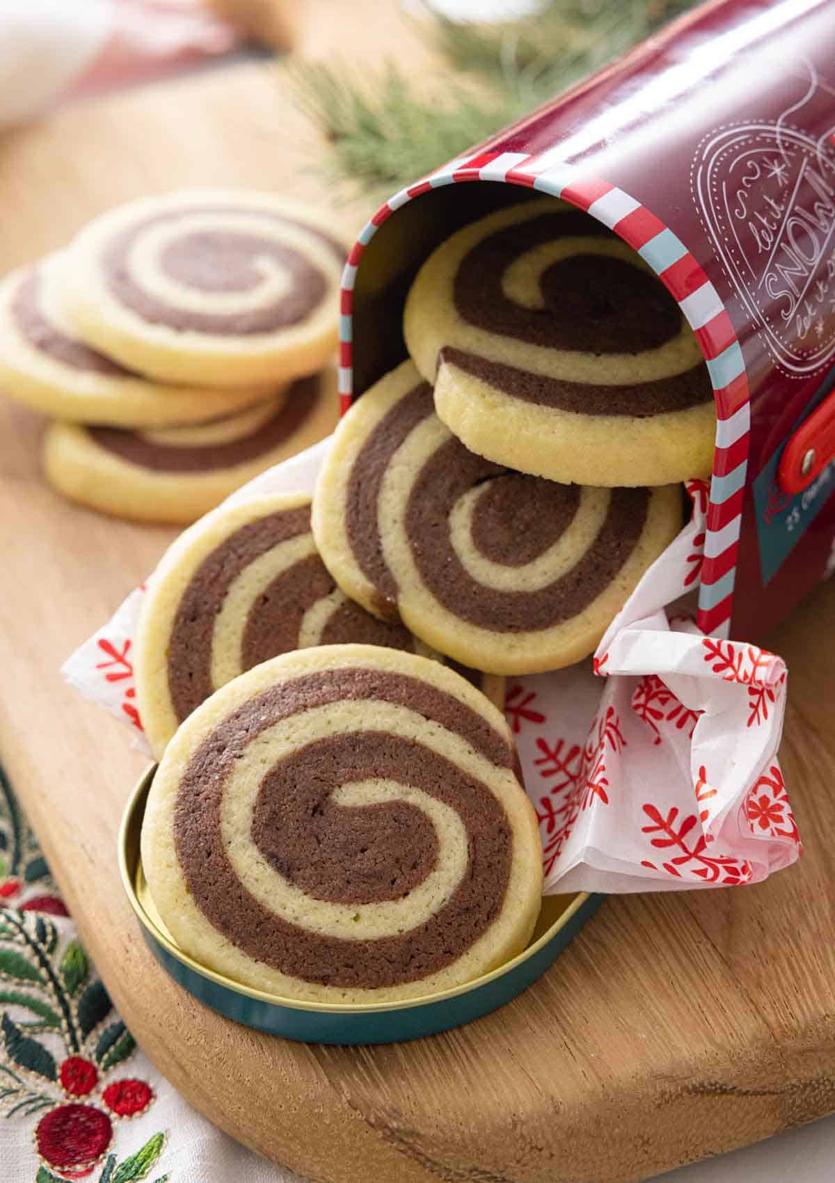 A Christmas tin with pinwheel cookies coming out of it.